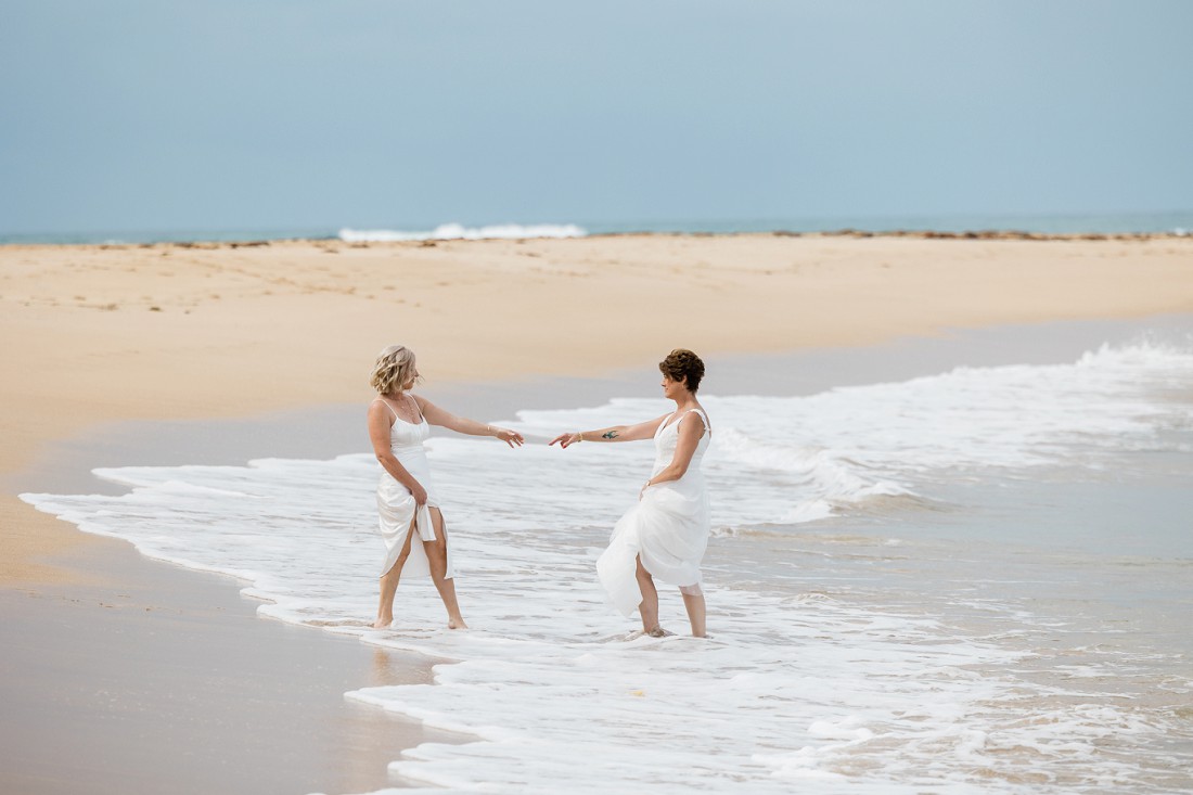 2 brides at the beach having fun in the ocean